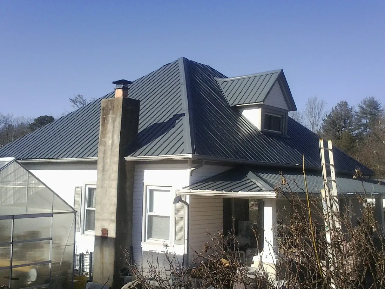 Dark blue standing seam metal roof on a white farmhouse with dormer — Slate & Tile Roof Repair by Roofing Brothers in Carolina