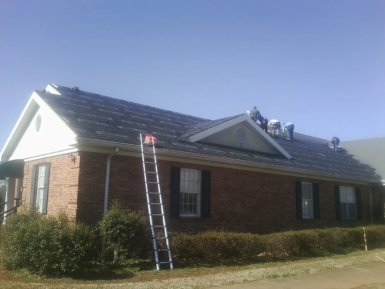Crew tearing shingles off a brick ranch roof with a ladder set — Emergency Roof Repair work by our crew in Carolina