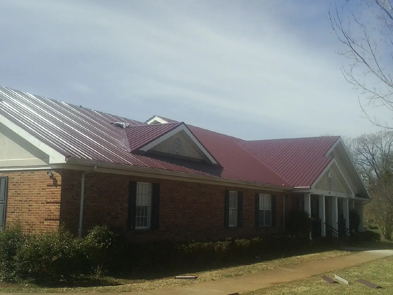 Red metal roof with gabled entries on a long brick building, from a Hail Damage Roof Repair job in Carolina