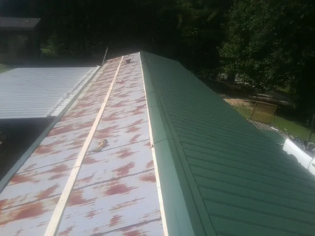Old rusted panels beside newly installed green metal roofing — Wind Damage Roof Repair by Roofing Brothers in Carolina