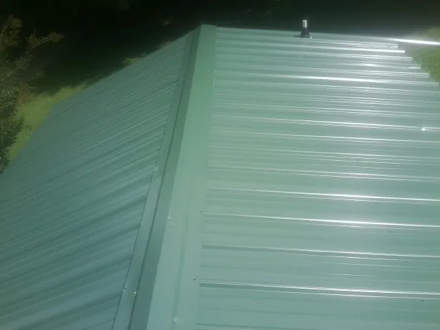 New green metal panels meeting at the ridge of a roof — Flat Roof Repair work by our crew in Carolina
