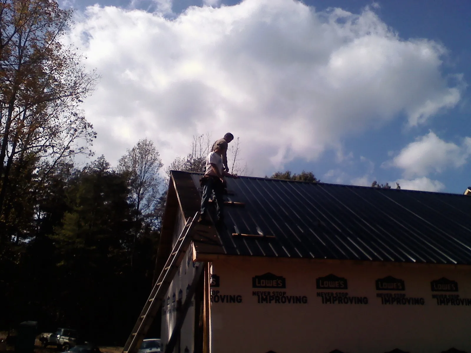 Roofer fastening dark metal panels high against a cloudy sky, from a Roof Inspection job in Carolina