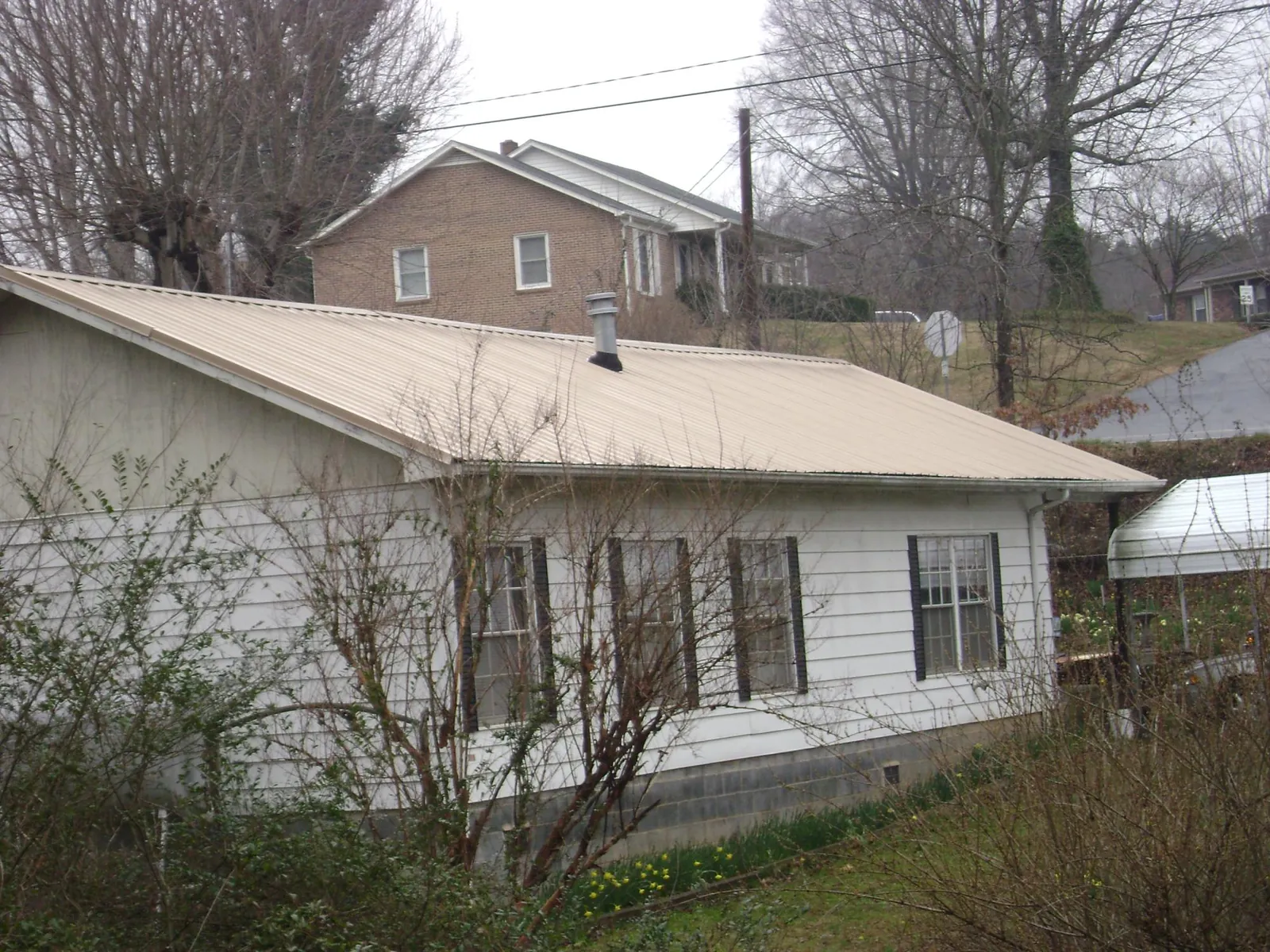 Tan metal roof on a white sided house set into a hillside — Commercial Roofing by Roofing Brothers in Carolina